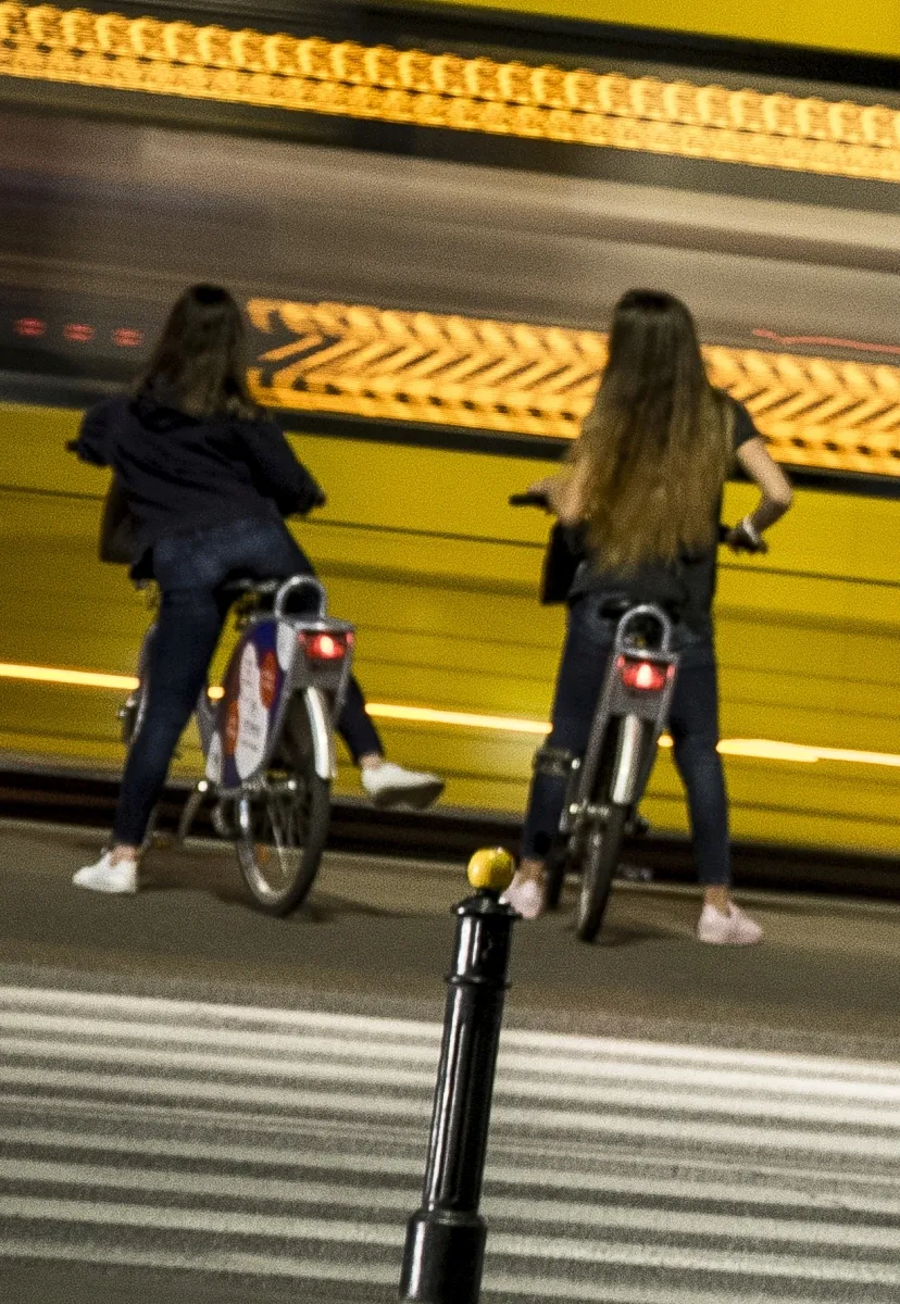 Two women stopped on bicycles with a yellow tram behind them